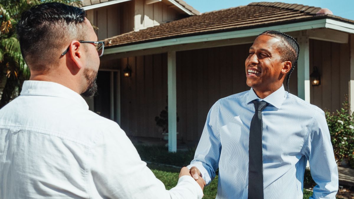 Two buyers shaking hands in front of a new property